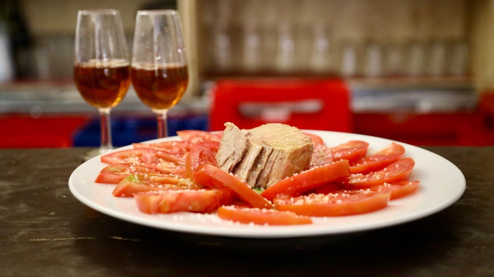 Plato de tomate con atún acompañado de vino.