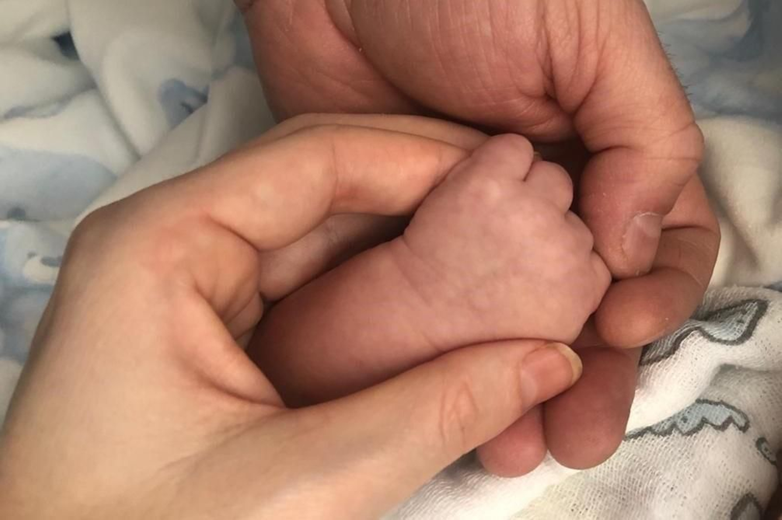 Las manos de Manme y Francisco rodean la pequeñita mano de su bebé, que crece sano.