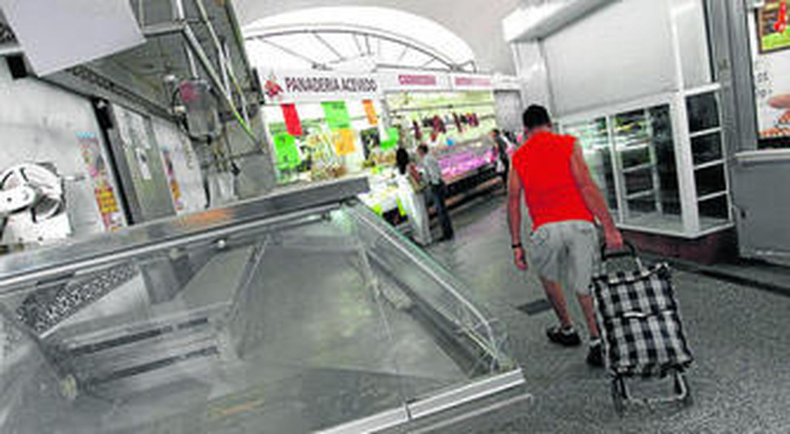 Un hombre empuja un carro de compra en el interior del mercado de abastos entre dos puestos cerrados.