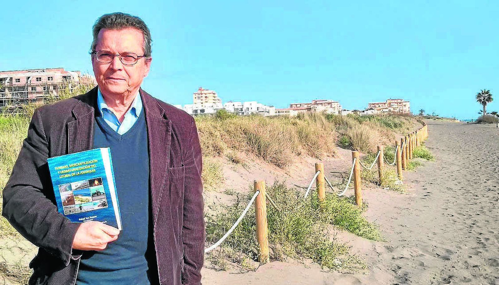 Rafael Yus posa para esta entrevista con su libro junto a las dunas de El Morche.