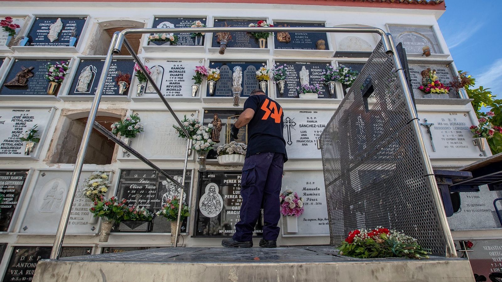 Uno de los encargados de mantenimiento del cementerio repone flores en uno de los nichos más elevados.