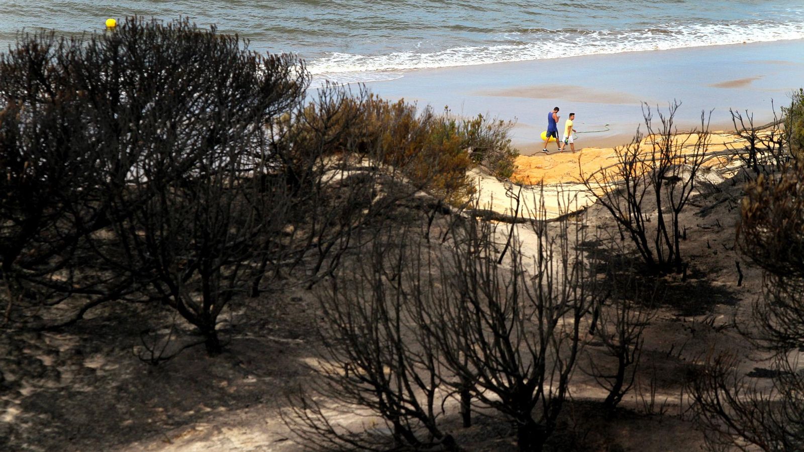 Dos personas pasean por la playa cerca de la zona incendiada.