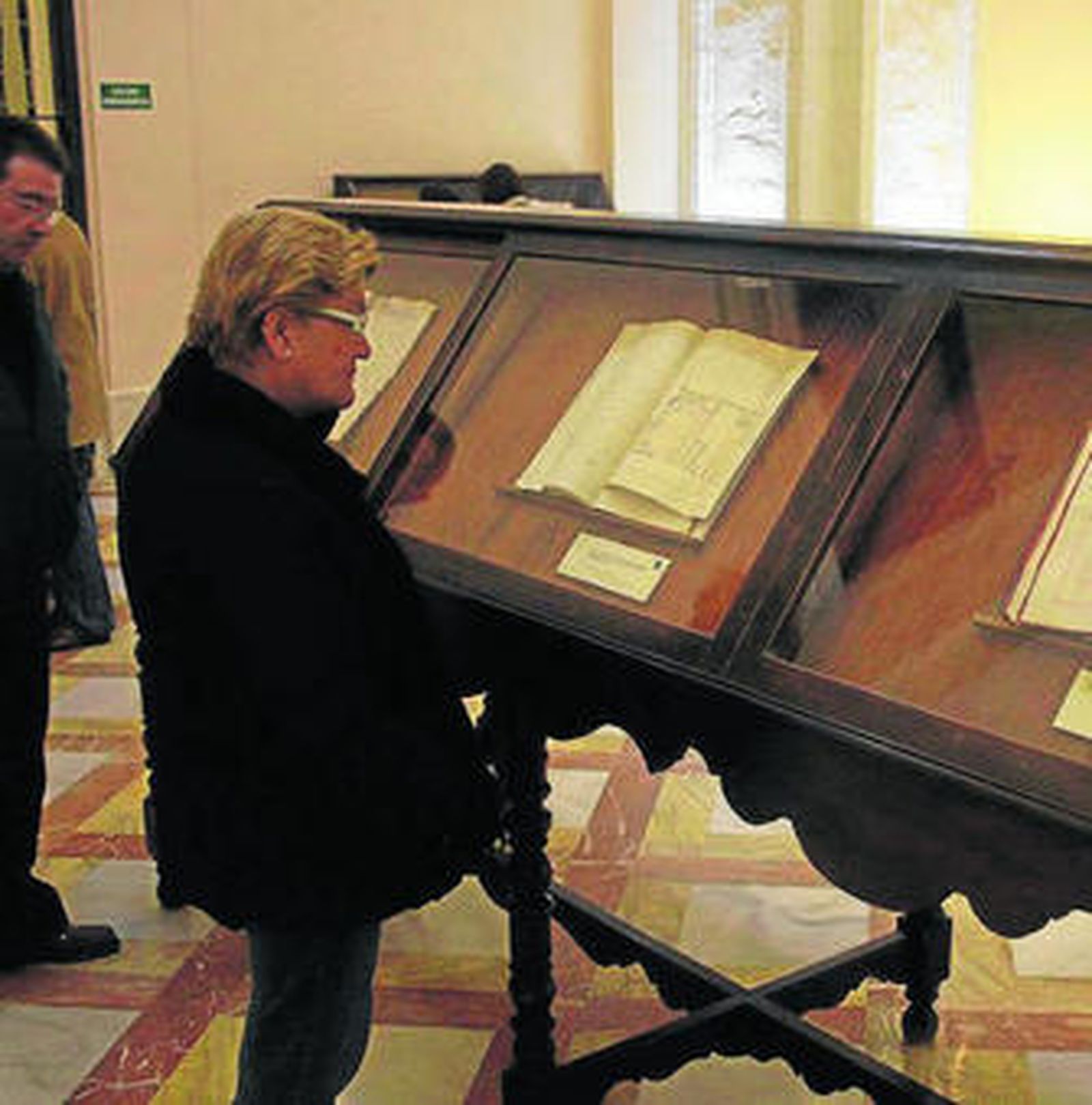 Una mujer mira el plano de un caserío, junto al testamento de Mañara.