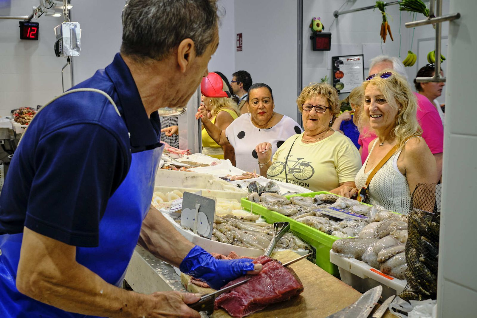 Un pescadero en pleno corte ante las atentas miradas de unas clientes.