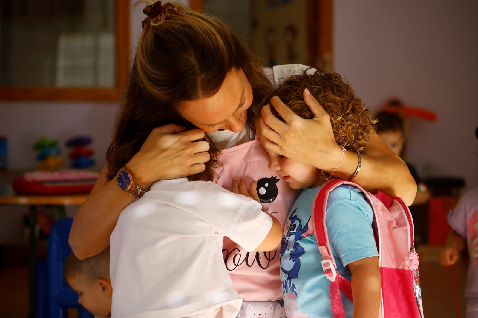 Una docente de la escuela infantil Santuario abraza a varios alumnos.