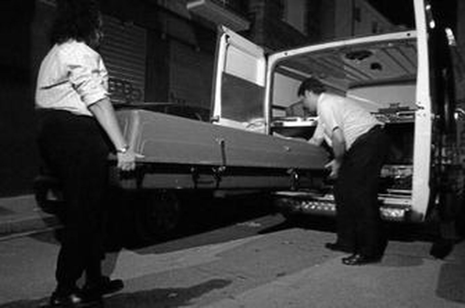 Los servicios funerarios introducen el féretro con el fallecido en el furgón a la salida del edificio afectado.