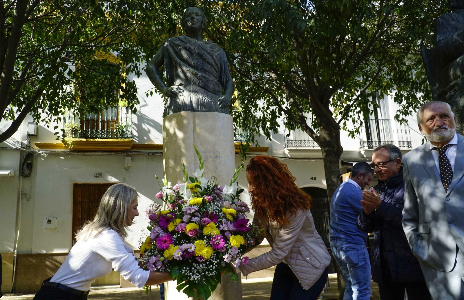 Patricia del Pozo, consejera de Cultura de la Junta, y Clara Macías, delegada del Ayuntamiento en el distrito Macarena, depositan el ramo de flores junto a la estatua de  la Niña de los Peines.