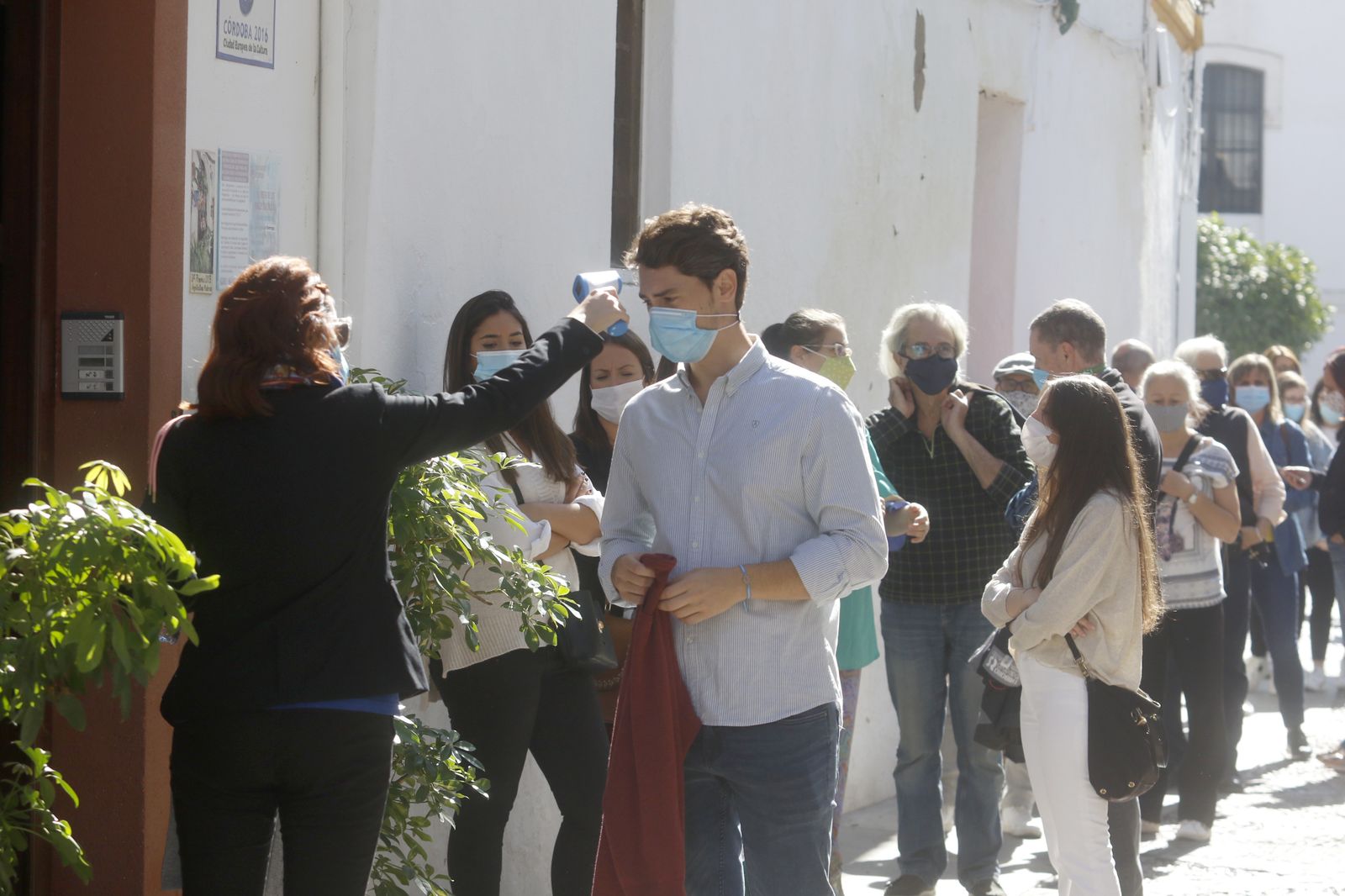 Una controladora toma la temperatura a un visitante en la entrada a un patio.