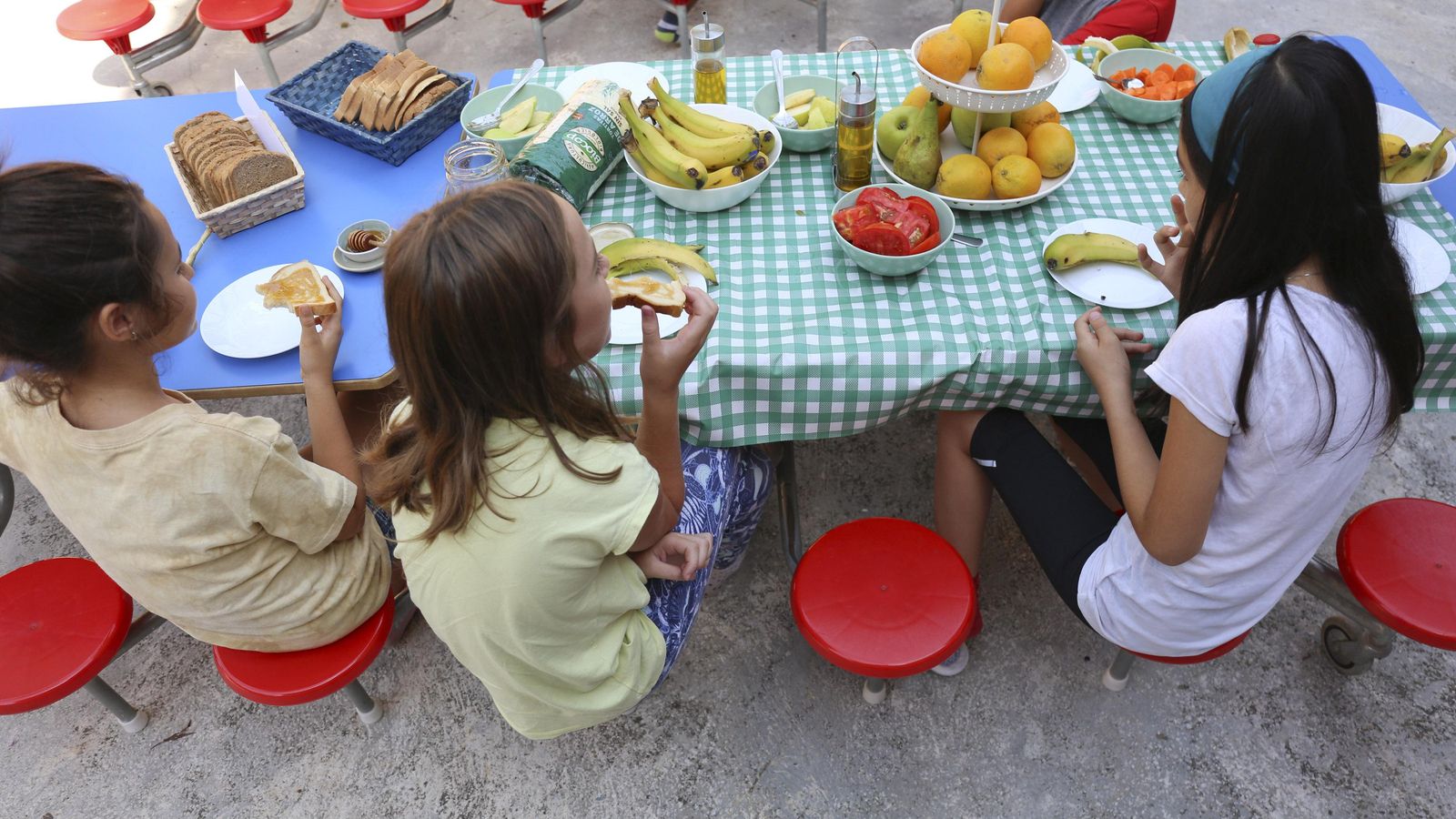 Tres alumnas hacen el desayuno a base de pan y fruta.