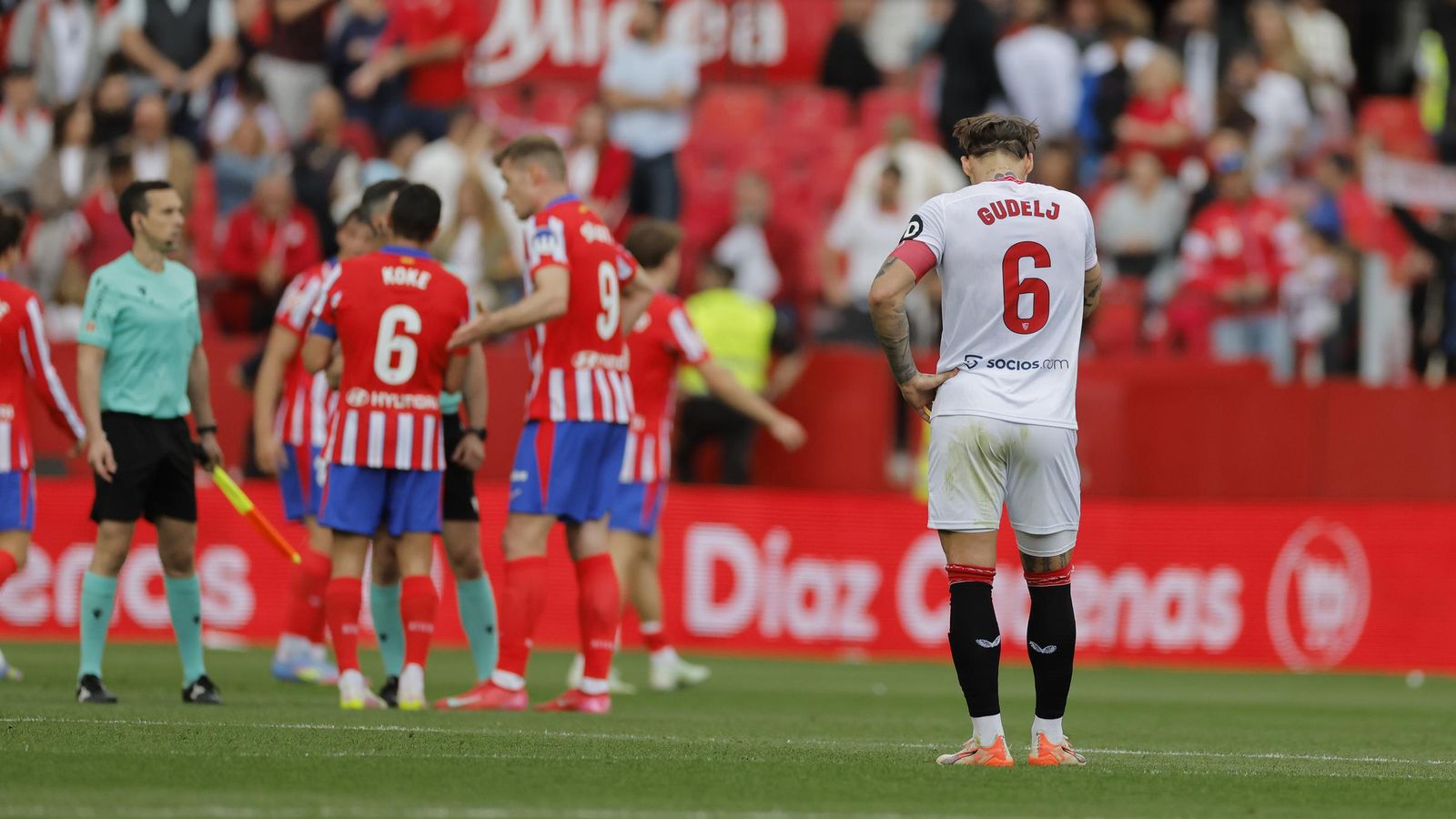 Gudelj agacha la cabeza cabizbajo mientras los futbolistas del Atlético celebran el triunfo.