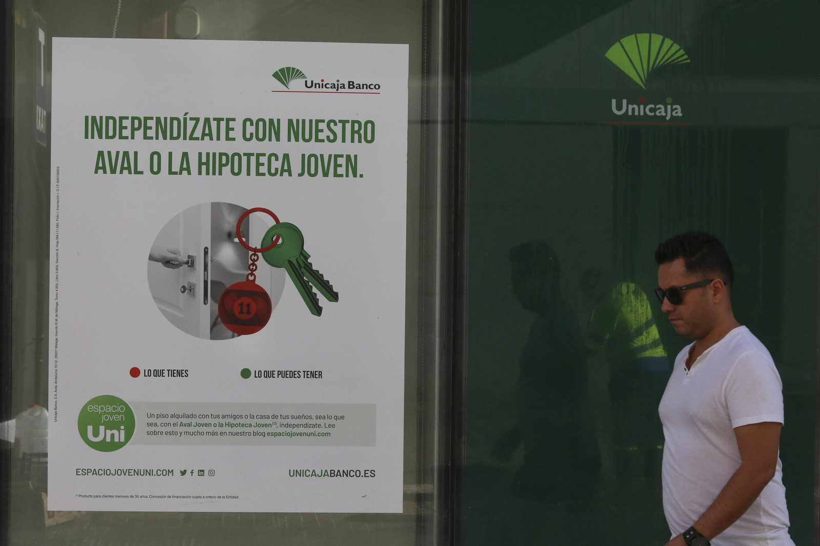 Un hombre pasa junto a una oficina de Unicaja Banco con un anuncio de una hipoteca.