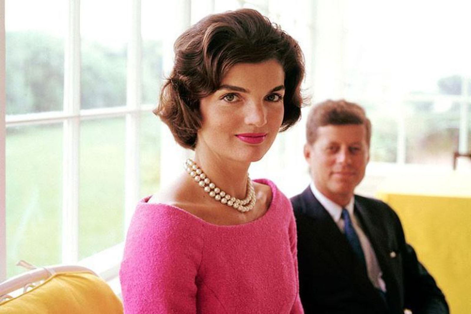 Jackeline Kennedy (JFK en segundo plano), con vestido fucsia y collar de perlas.