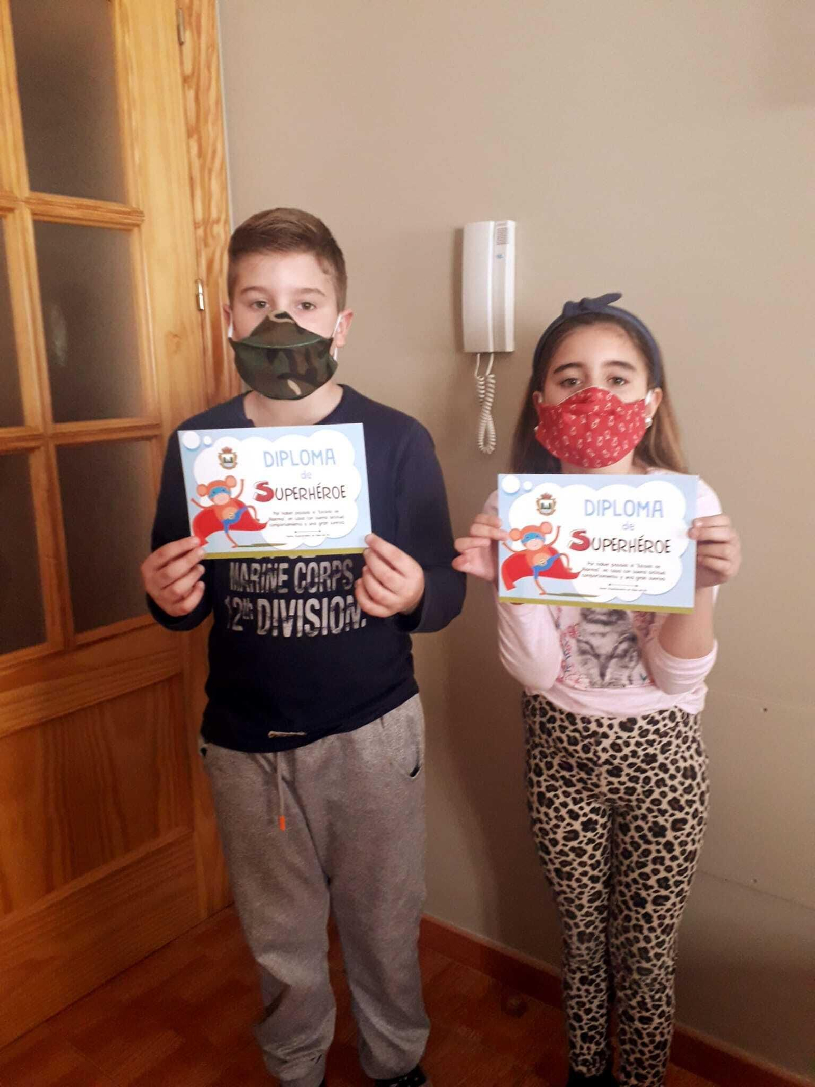 Los pequeños Álvaro y Martina muestran orgullosos sus diplomas de buen comportamiento y las mascarillas con motivos infantiles