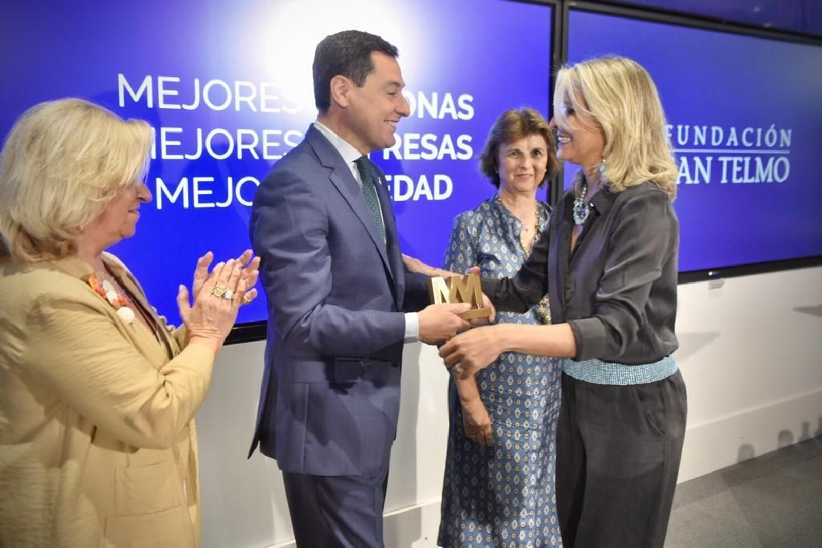 Juanma Moreno entrega el galardón a Claudia Hernández Rodríguez en presencia de Irene Navarro, presidenta de Ammde (a la derecha), y Rocío Medina, directora de la asociación en Andalucía Occidental