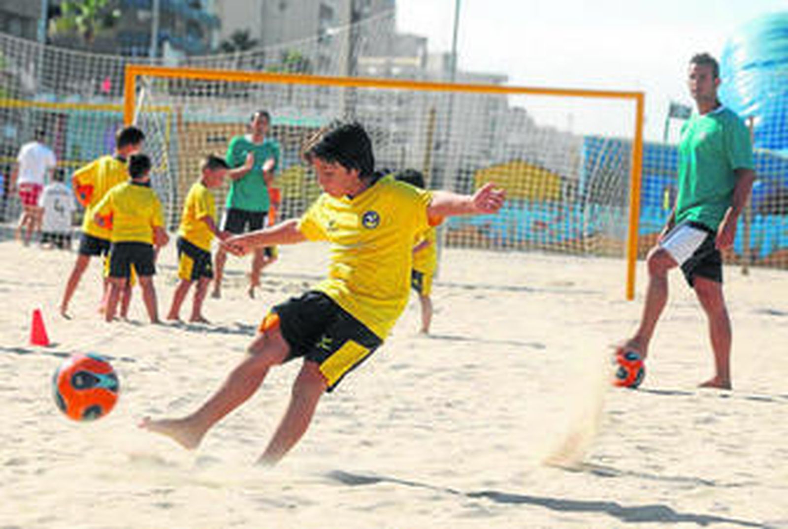Uno de los alumnos de la escuela de fútbol-playa realiza un disparo ante la mirada de un monitor.