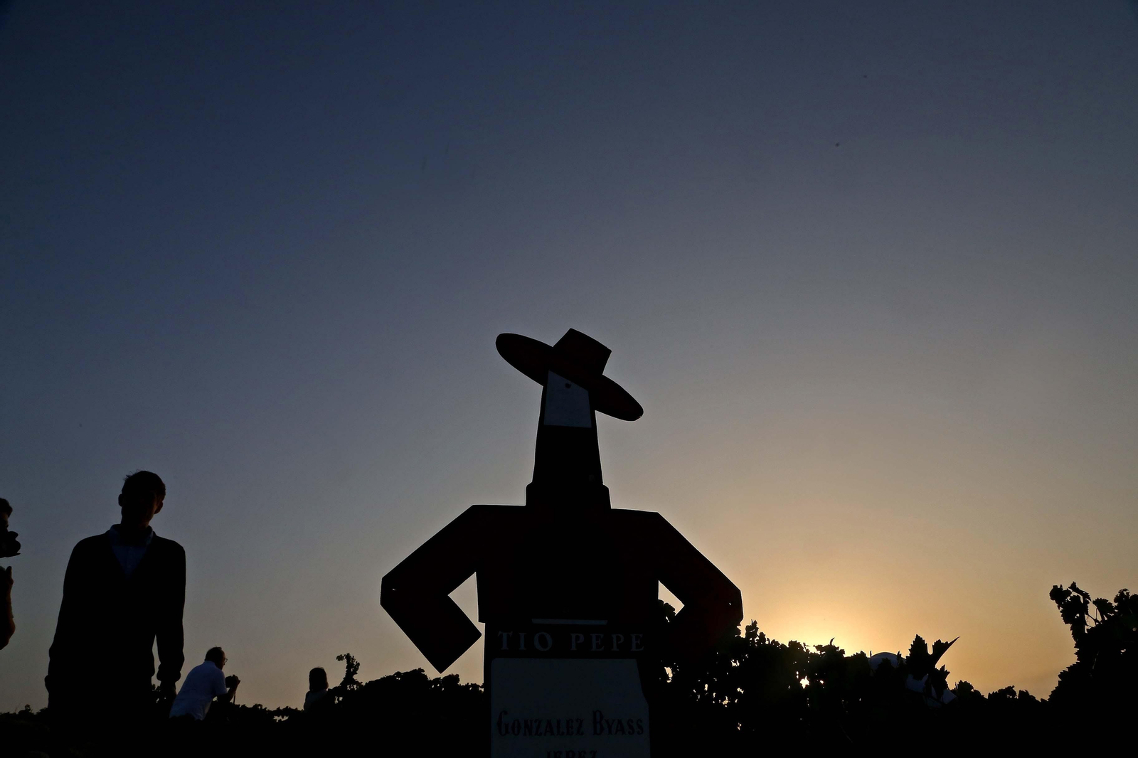 Silueta de varios vendimiadores mientras comenzaba a amanecer junto al emblema de la bodega, el Tío Pepe, en la viña 'La Racha'.