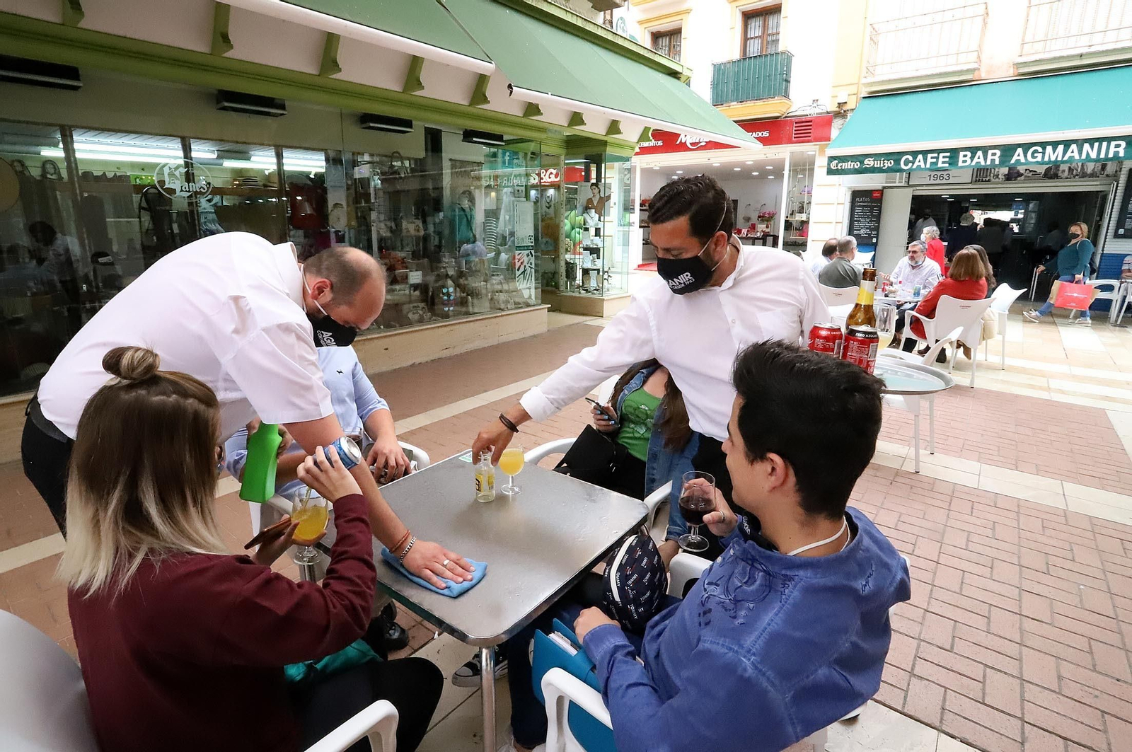 Un camarero desinfecta la mesa para que un grupo de amigos pueda sentarse en la terraza de un bar.