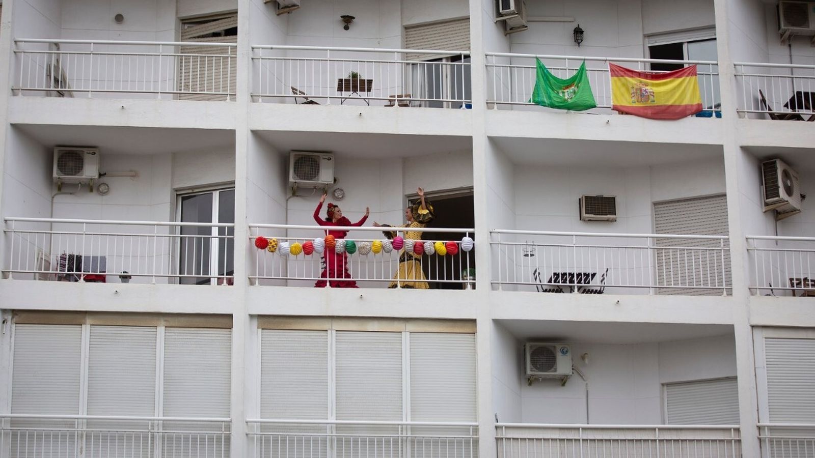 Las jóvenes bailan sevillanas desde su balcón decorado con farolillos.