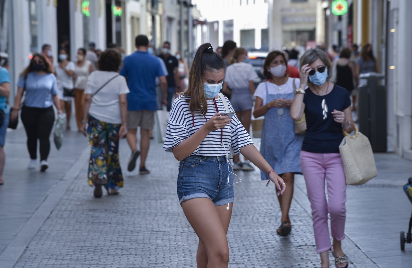 Una chica joven mira el móvil mientras camina por una abarrotada calle del centro de Sevilla.