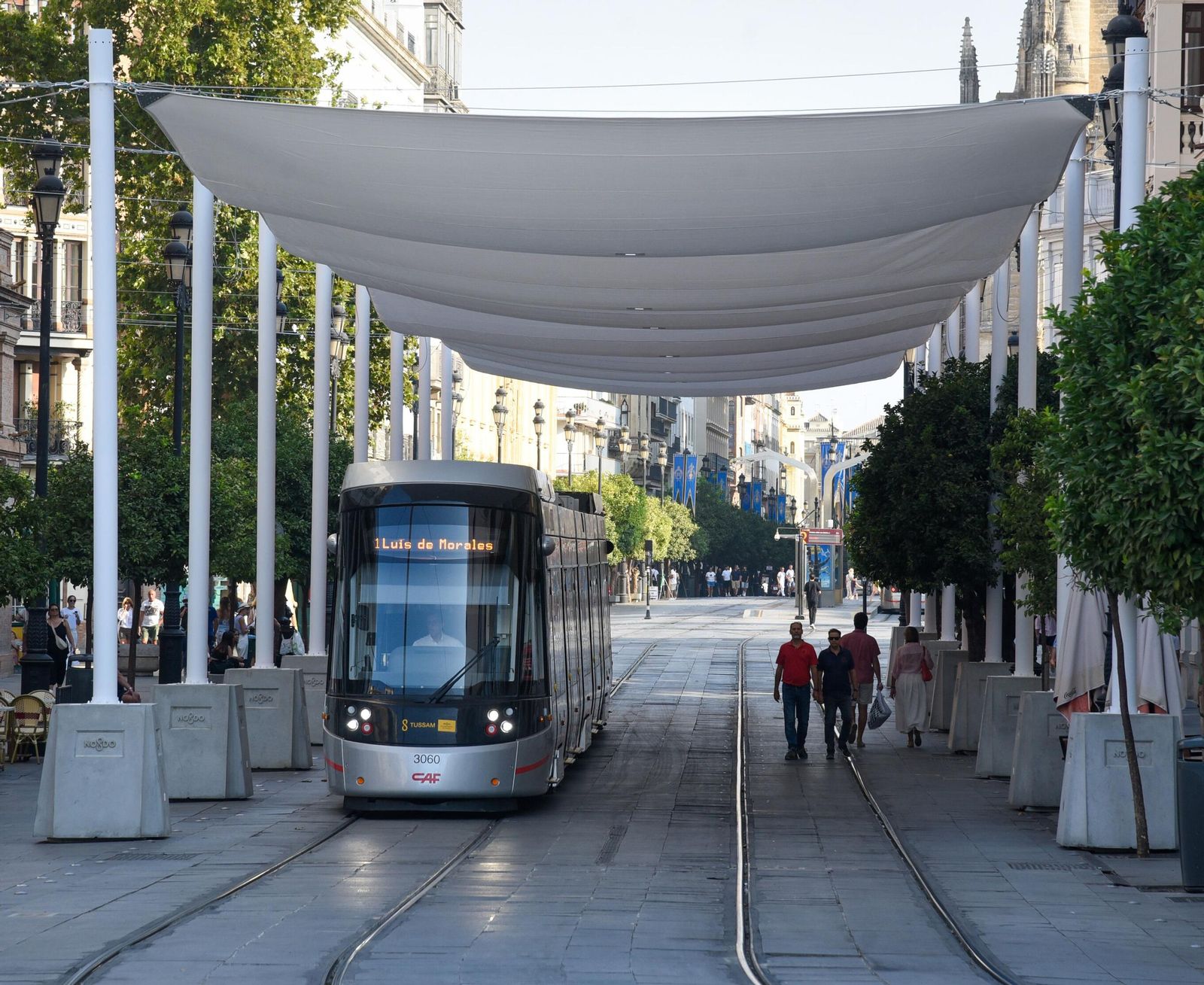 El tranvía y algunas personas comparten el espacio bajo las velas.