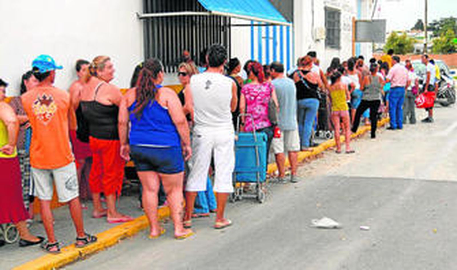 Fila de personas para recoger productos alimenticios, frente a un local que ocupa Cruz Roja junto al Puente Azul.