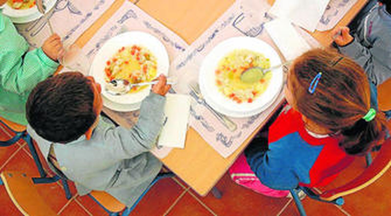 Niños ante sus platos de sopa en un comedor escolar.