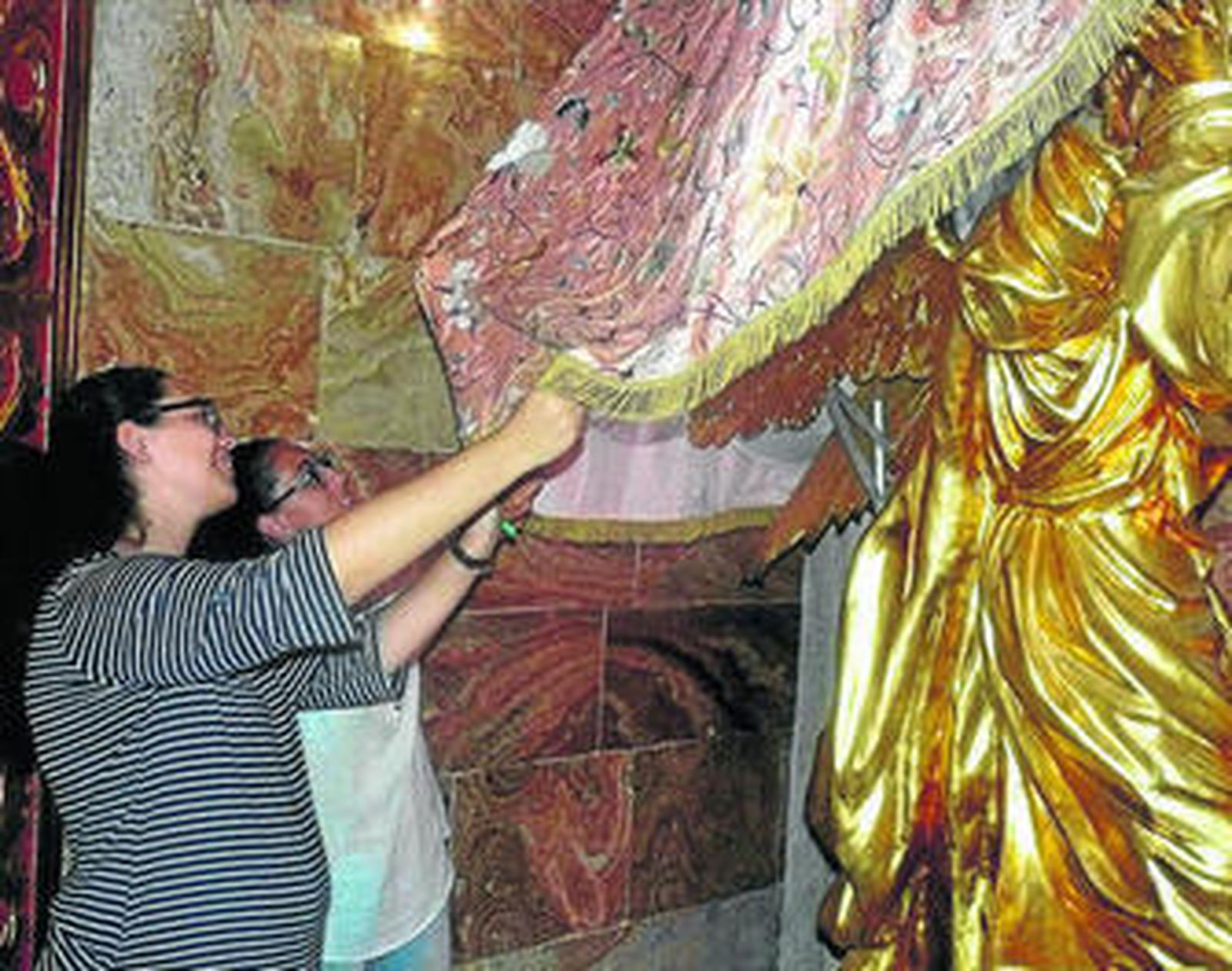 Dos de las camareras revisan el manton de la Virgen del Mar en su camarín.
