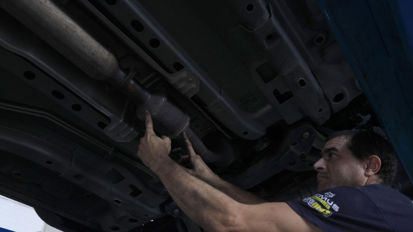 Un trabajador del taller explica dónde va el catalizador en los bajos del coche.