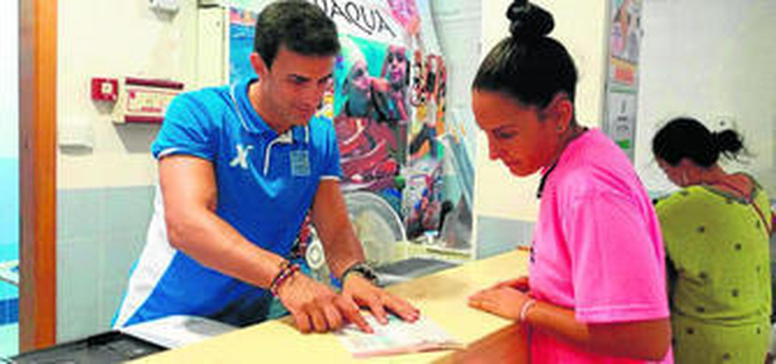 Marcos Roda, técnico de la piscina, en la recepción del centro ofrece a una usuaria información del programa.