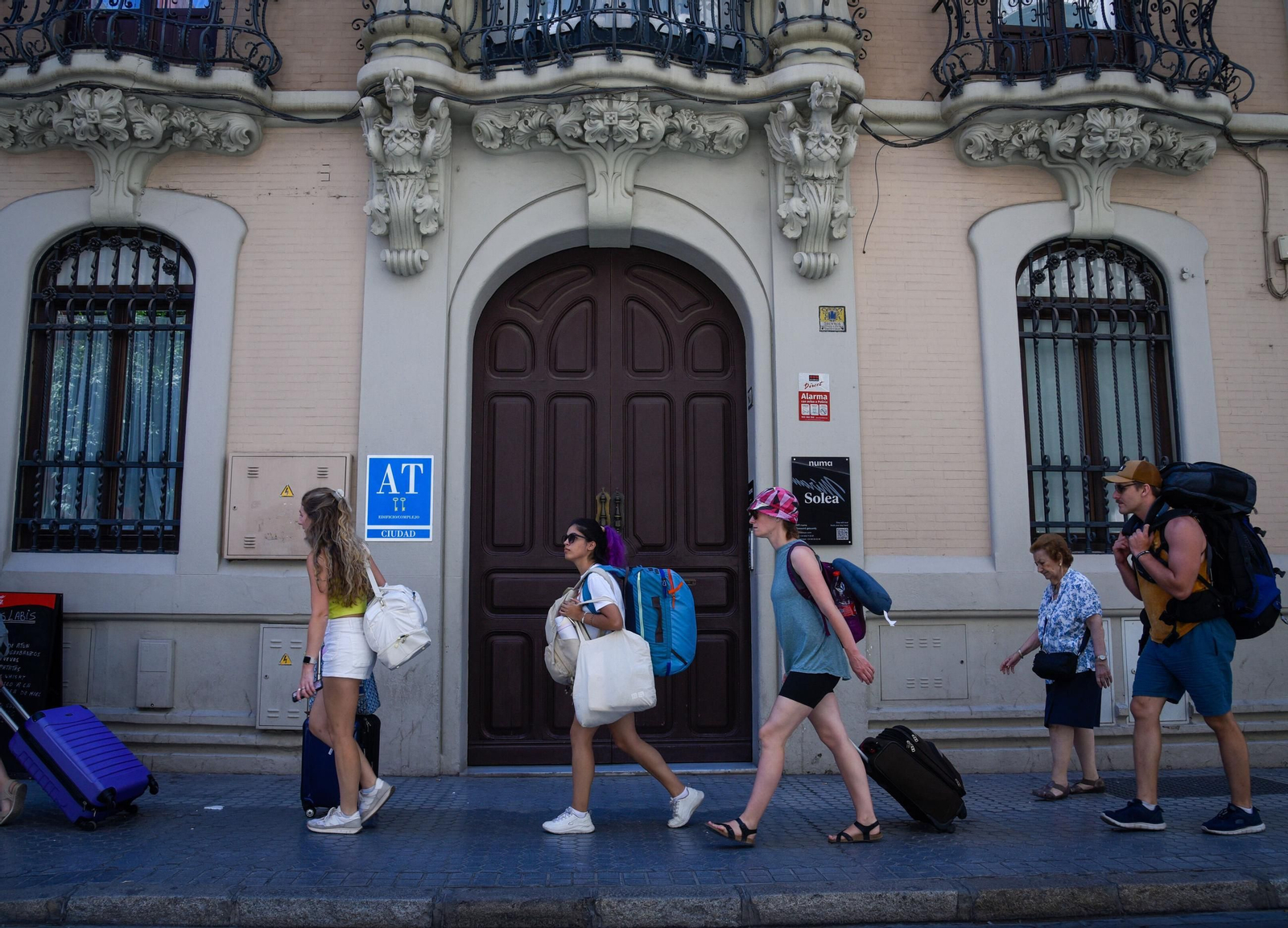 Un grupo de turistas arrastran sus maletas por delante de un alojamiento turístico.