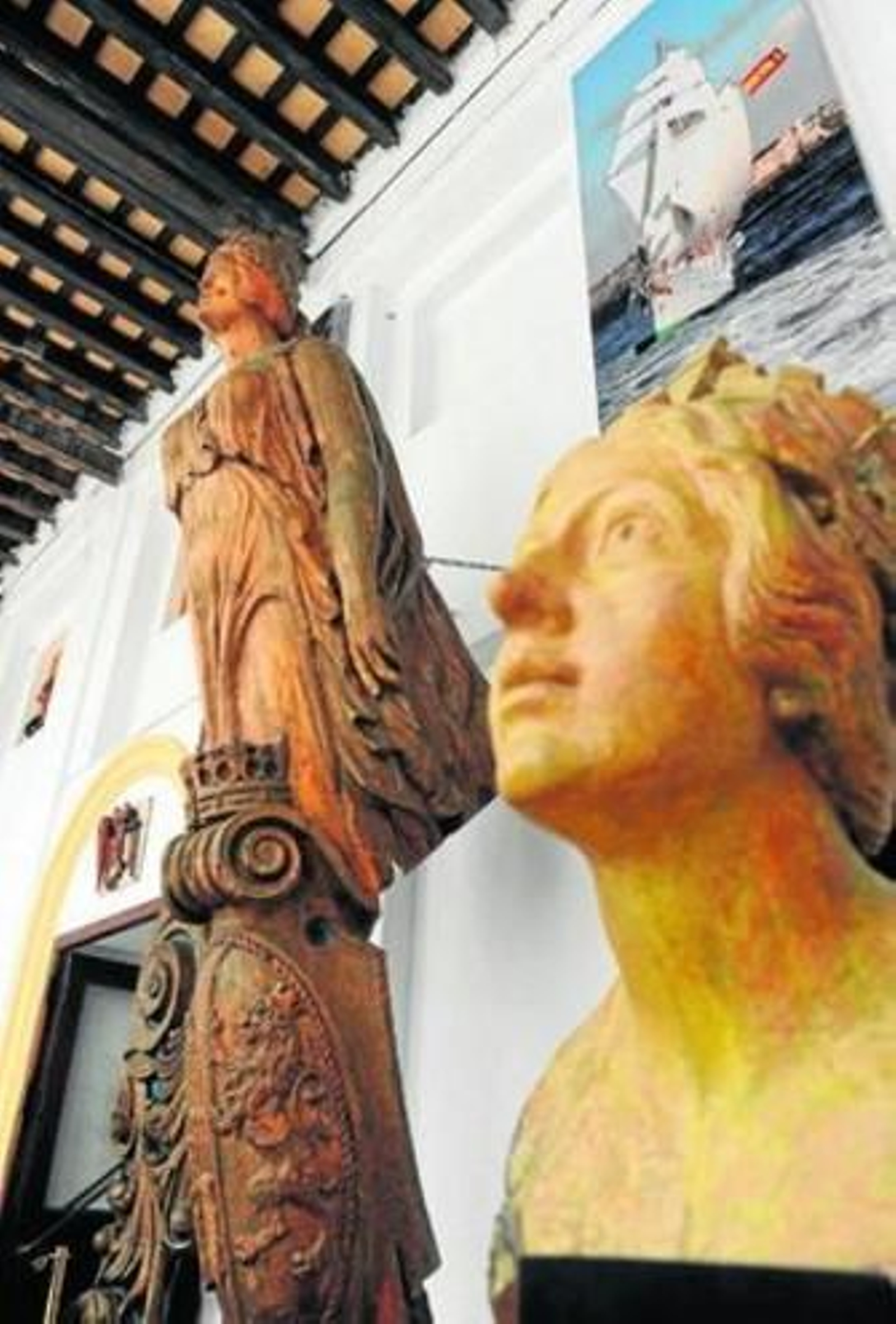 La cabeza originaria del primer mascarón de proa y al fondo, el propio mascarón, ahora rehabilitado.