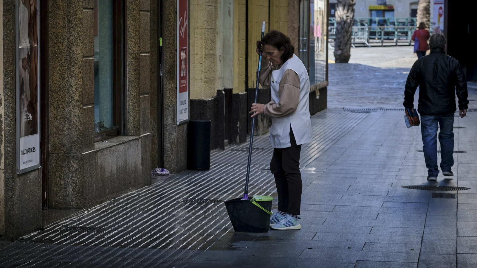 una mujer limpia la acera de una óptica en la calle Pelota
